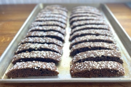 Sliced biscotti standing on end on a parchment-lined baking sheet, just out of the oven.